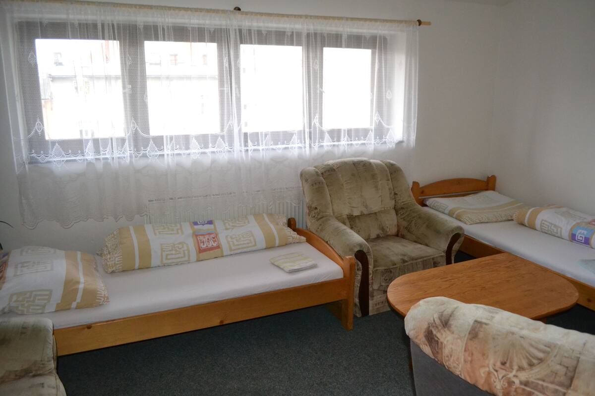 A dormitory room with two single beds, a wooden armchair, and a small table.
