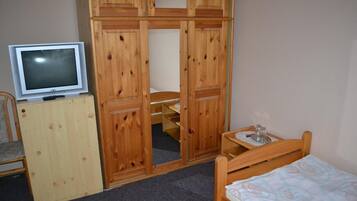 Un dormitorio con un armario de madera, una cama, una mesita con una bandeja y un televisor sobre un mueble.