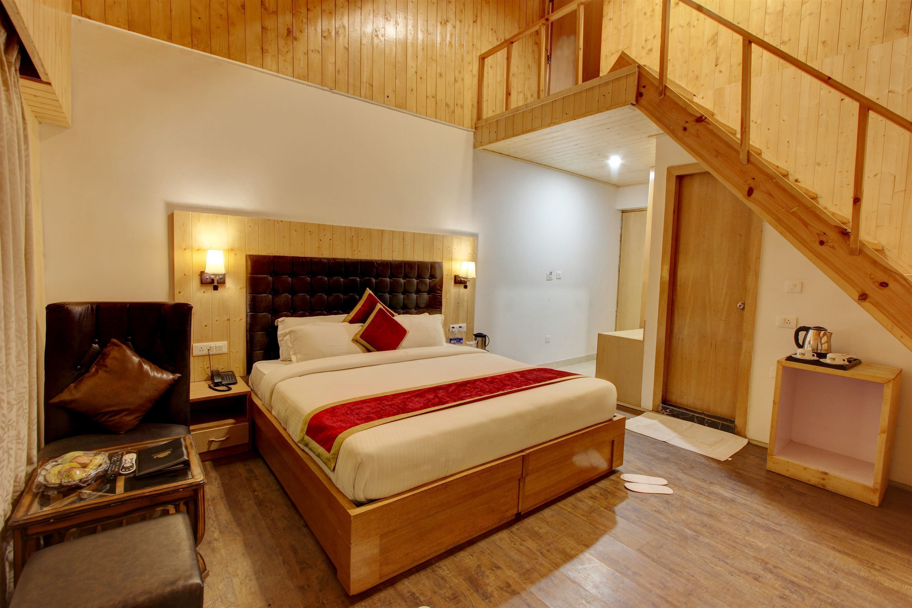 A bedroom with a large bed, wooden headboard, bedside lamps, a nightstand, a chair, and a wooden staircase.