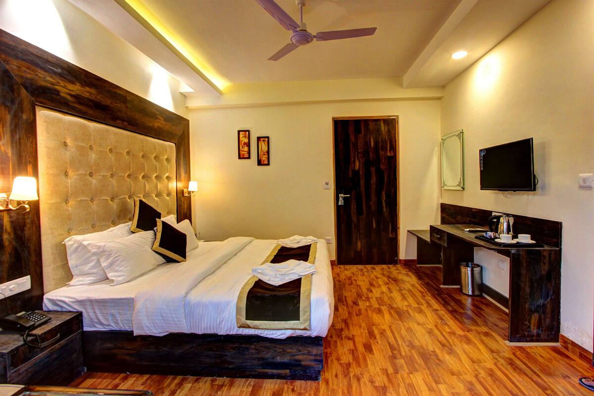 A hotel room with a large bed, a desk, a TV, and a ceiling fan.