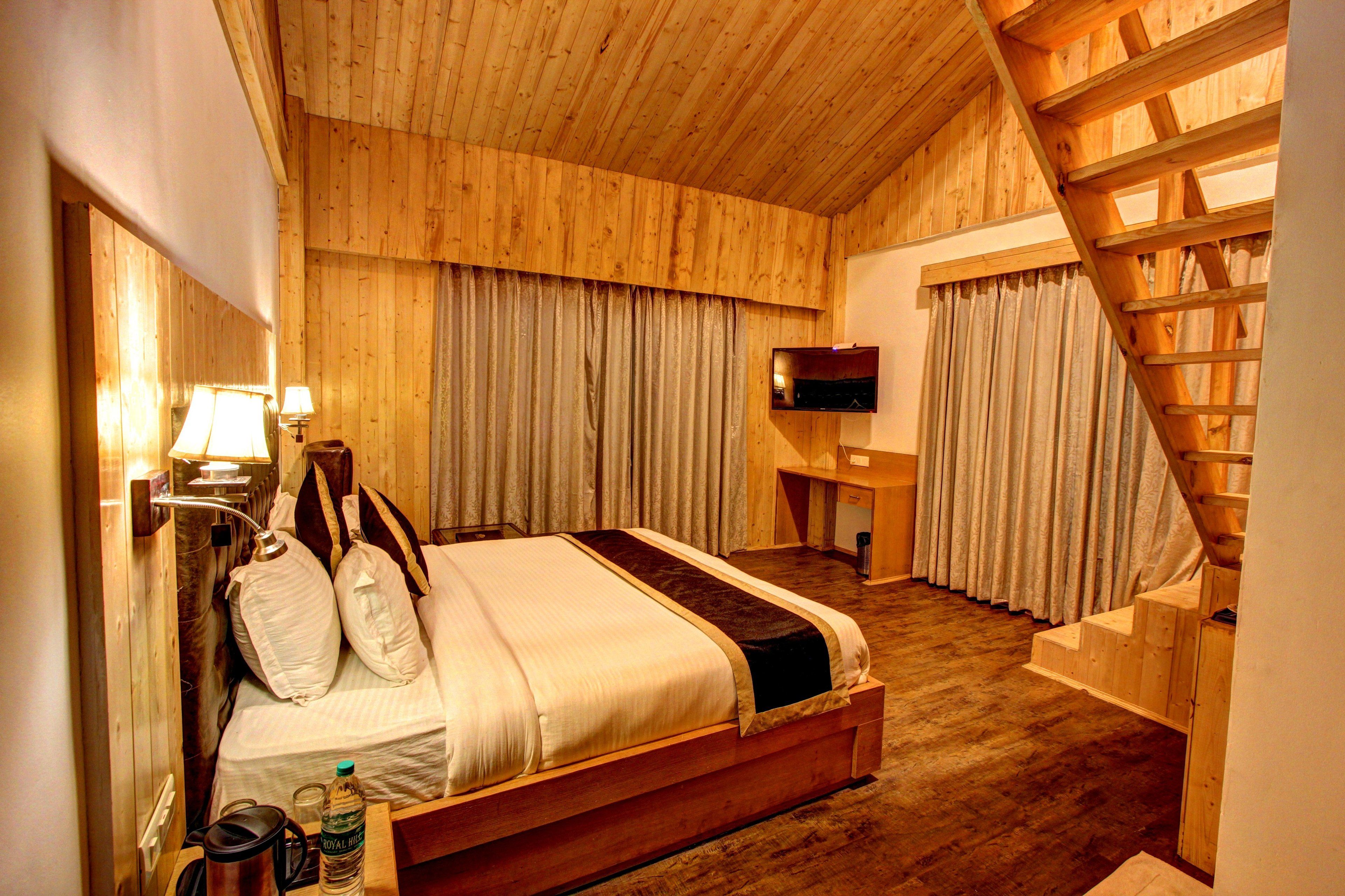 A wooden-paneled bedroom with a bed, a desk, a TV, and a staircase.