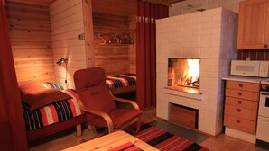 A cozy cabin interior with a bed, a chair, a fireplace, a microwave, and wooden cabinets. - Seita Cabins (Kolari)