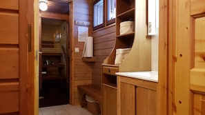 A wooden interior with a wooden bench, shelves with baskets, a small table, and a door leading to another room. - Seita Cabins (Kolari)