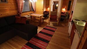 A cozy cabin interior with a wooden floor, a dining area, a kitchen with a sink, and a living room with a sofa and a fireplace. - Seita Cabins (Kolari)