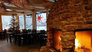A cozy restaurant with a stone fireplace, wooden tables, and chairs. - Seita Cabins (Kolari)