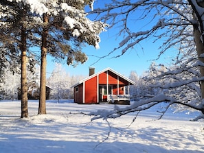 A cabin with a red exterior, surrounded by snow-covered trees and a clear blue sky. - Seita Cabins (Kolari)