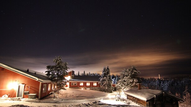 A snow-covered landscape with a wooden cabin and a red building with lights on. - Seita Cabins (Kolari)