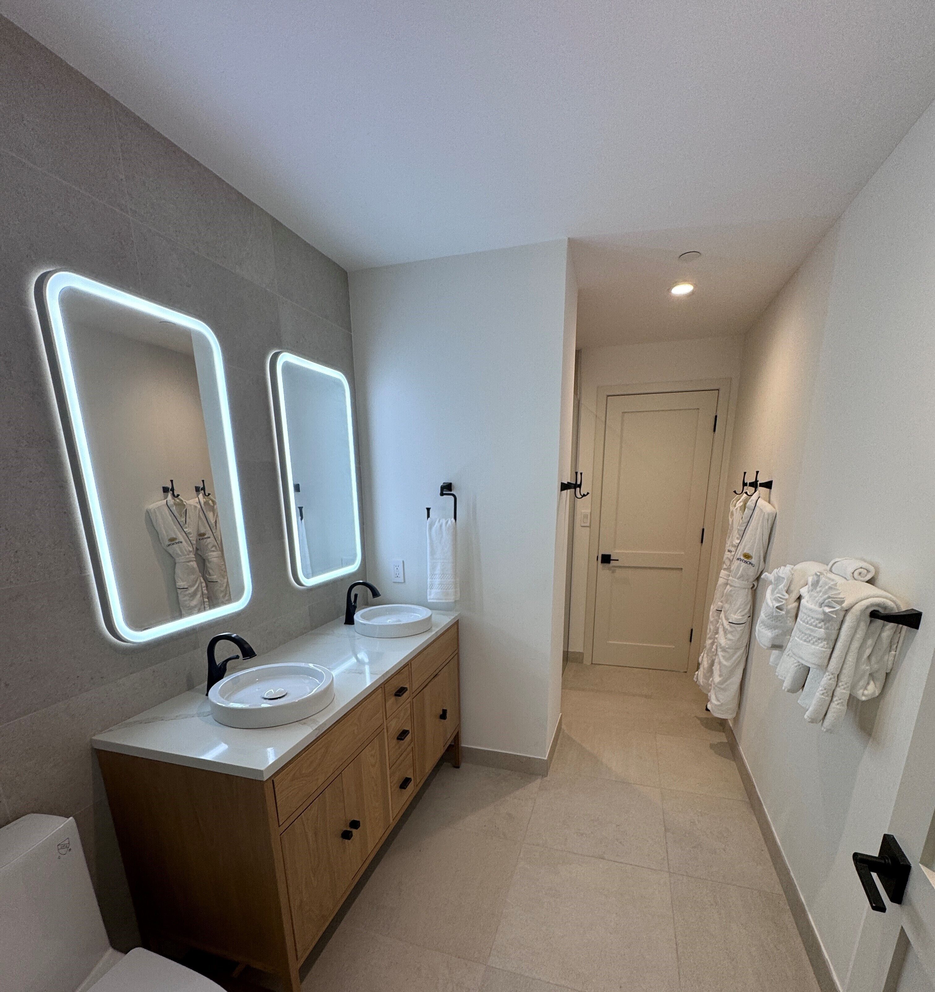 A modern bathroom with two sinks, a vanity, and a mirror with illuminated edges.