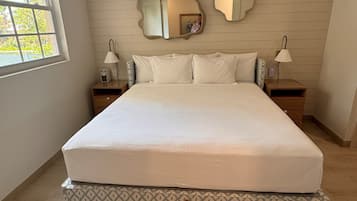 A neatly made bed in a room with a large window, two bedside tables with lamps, and two wall-mounted mirrors.