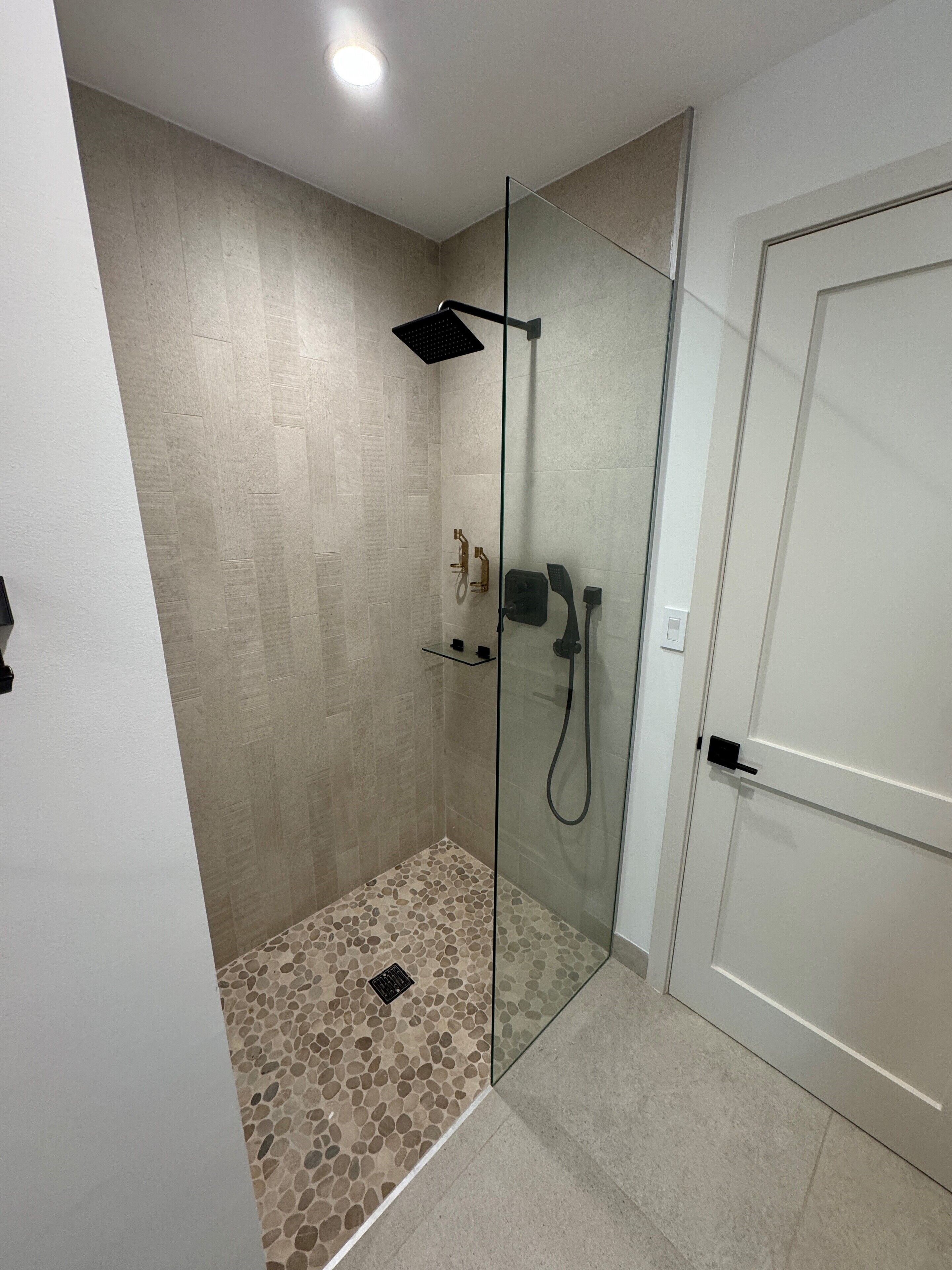 Une douche fermée par des parois en verre, avec un sol à motifs de galets, une douchette à main et un robinet mural.