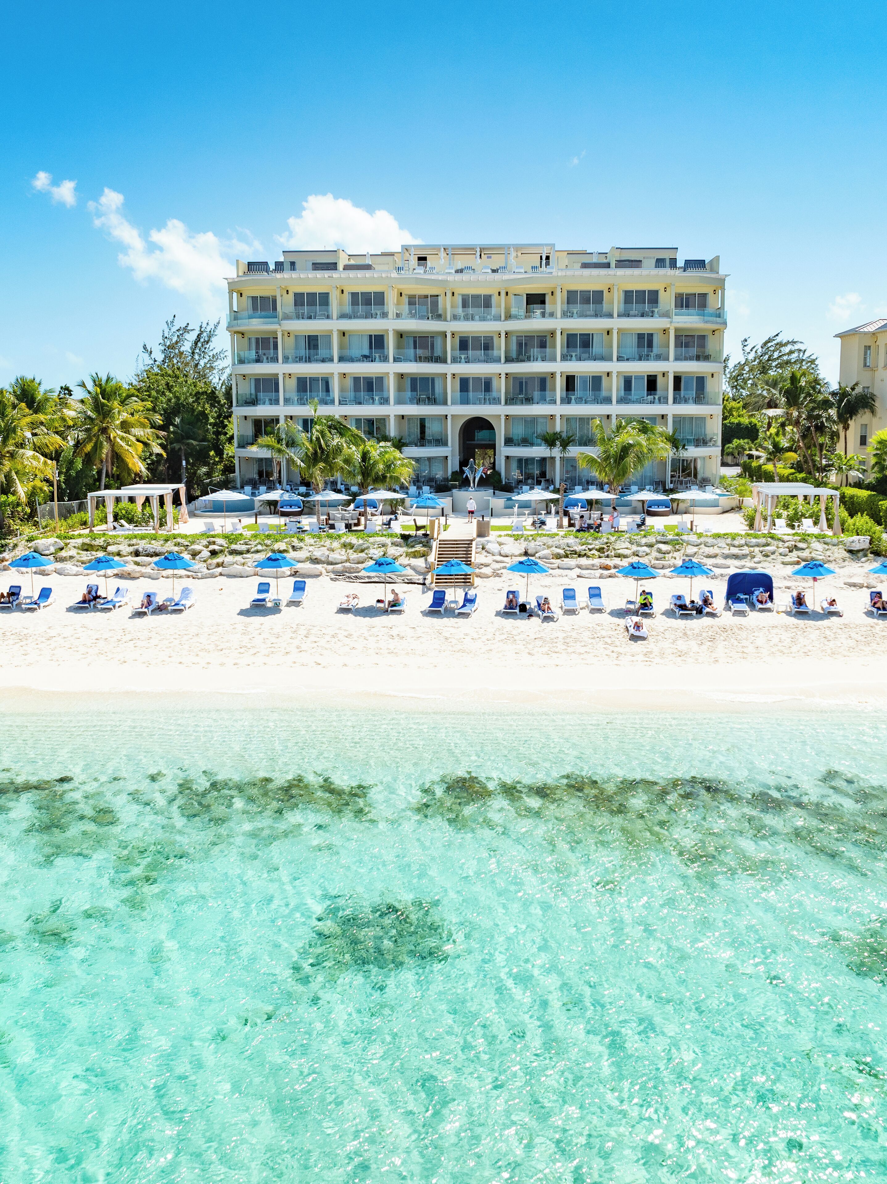 Ein Hotel mit mehreren Balkonen, einem Poolbereich mit Liegestühlen und Blick auf den Strand.