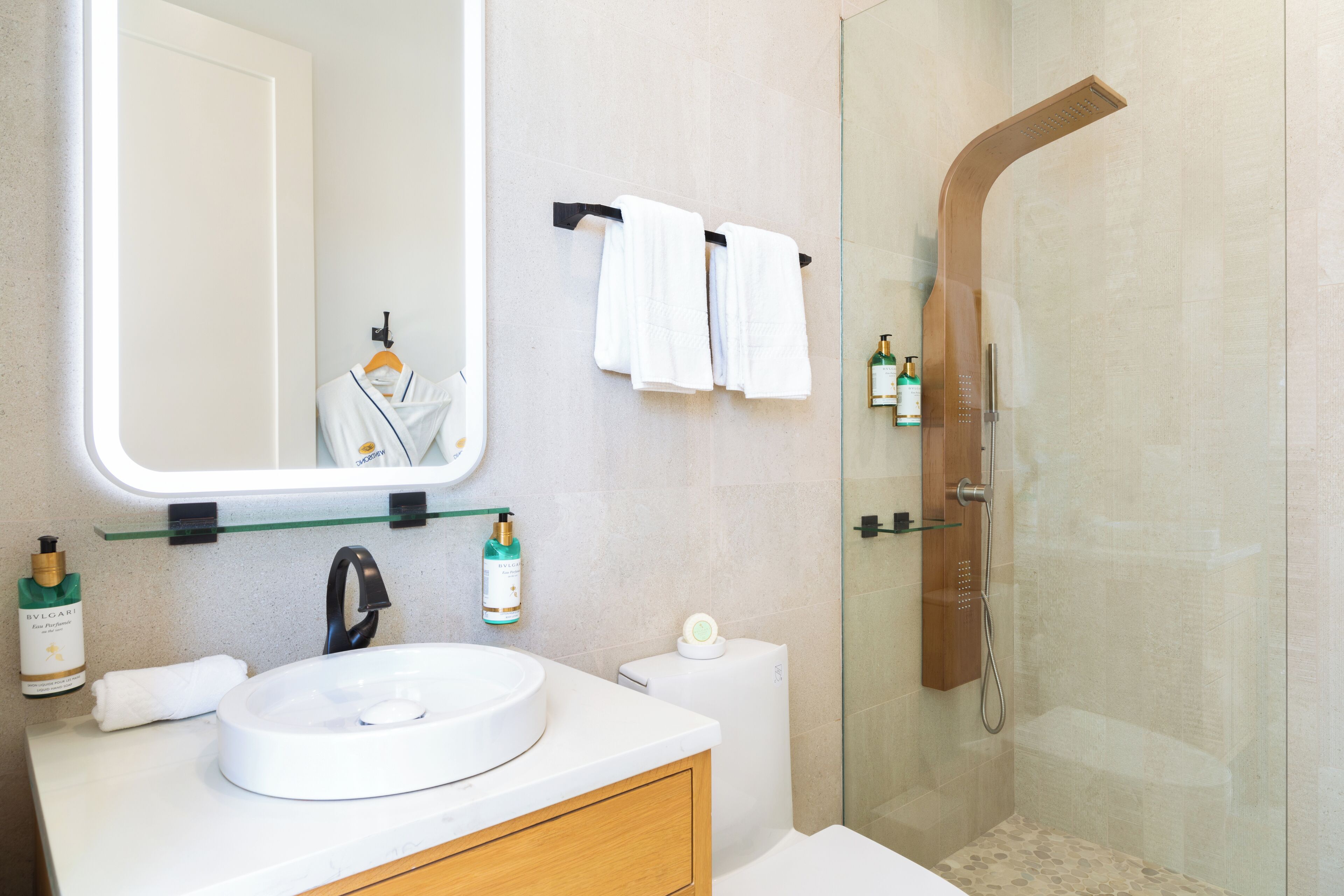 A modern bathroom with a round sink, a mirror, a toilet, and a shower enclosure.