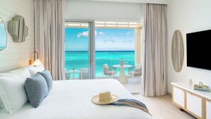 Habitación de hotel con cama, televisor, balcón con vista al océano y una mesa con sillas.