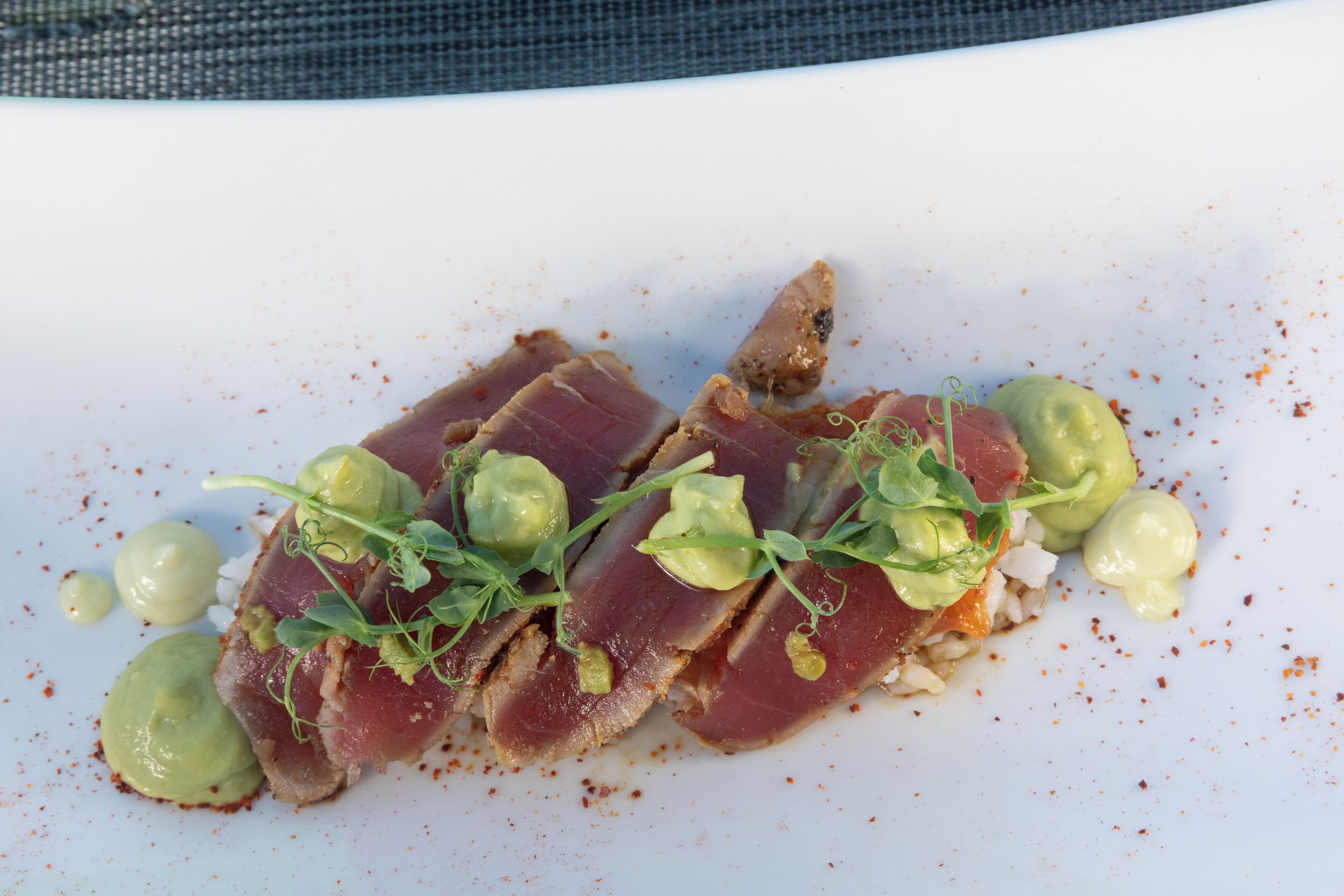 Un plato blanco con carne en rodajas, vegetales verdes y salsa cremosa.