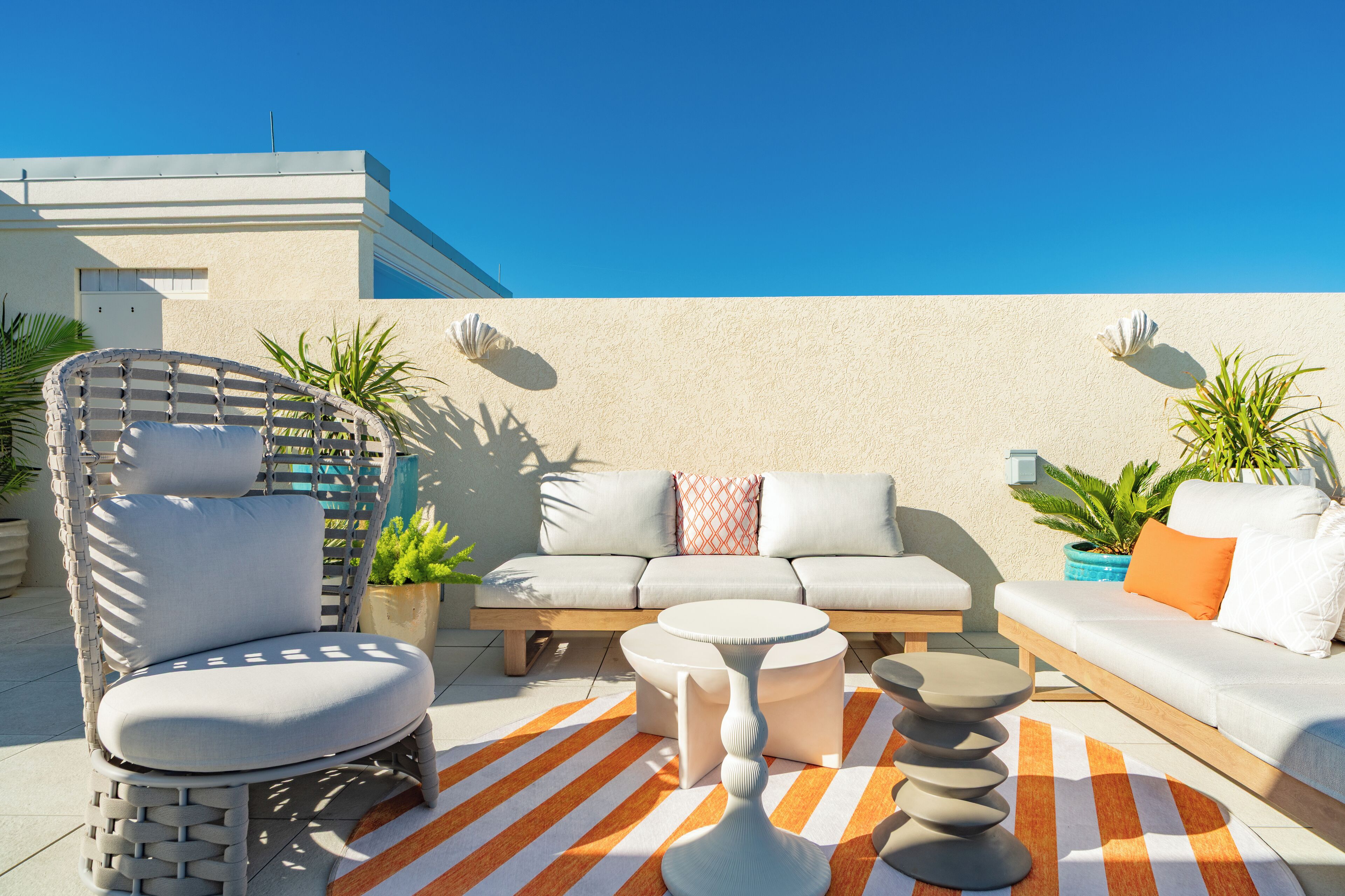 A modern outdoor seating area with a sofa, chairs, and a round table, surrounded by potted plants and a striped rug.