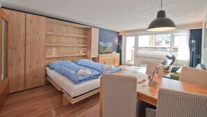 Una habitación con cama, armario de madera, mesa de comedor con sillas y vistas al exterior.