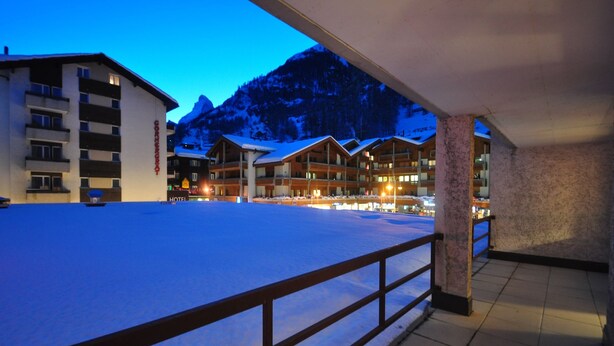 Un hotel de varios pisos, terreno cubierto de nieve y una montaña al fondo.