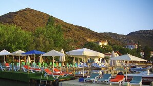 A waterfront resort with rows of sun loungers and umbrellas, a dock with boats, and a backdrop of hills. - Umut Otel & Beach (Marmaris)