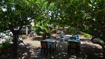 Un patio al aire libre con mesas y sillas de madera, rodeado de abundante vegetación y árboles.