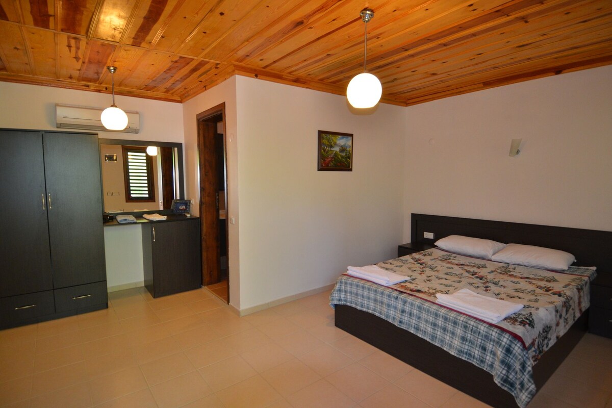 A bedroom with a wooden ceiling, a bed with a floral bedspread, a nightstand, and a wardrobe.