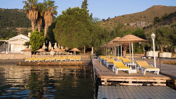 A wooden dock with lounge chairs and umbrellas, a pool, and a building with a white facade. - Umut Otel & Beach (Marmaris)