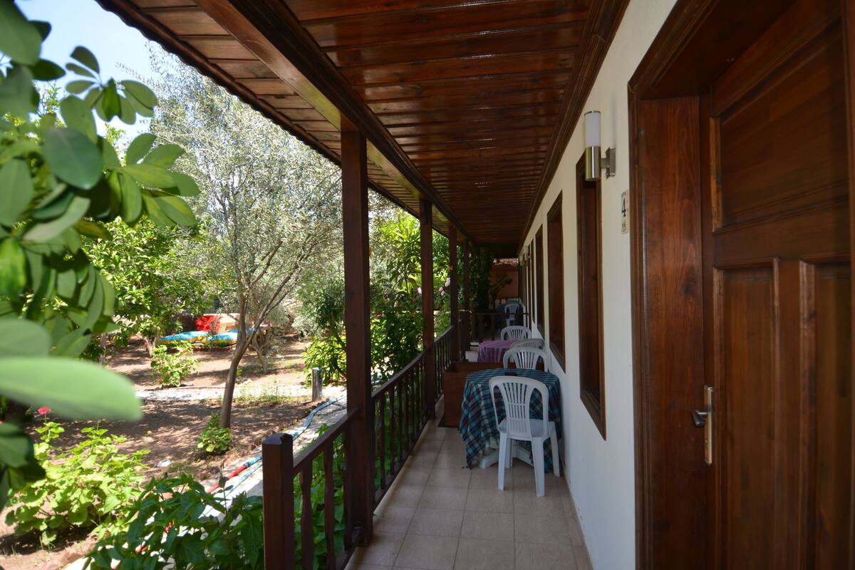 A covered porch with a wooden ceiling, a table with chairs, and a view of a garden with trees and a blue car.