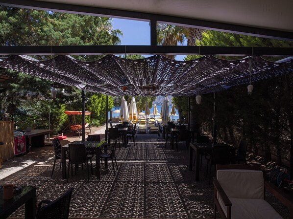 An outdoor seating area with tables and chairs, covered by a patterned canopy, and overlooking a beach. - Umut Otel & Beach (Marmaris)