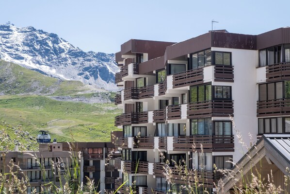 A modern multi-story hotel with balconies, set against a backdrop of snow-capped mountains.