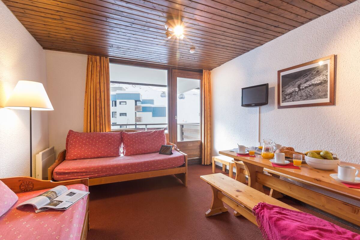 Ein gemütliches Zimmer mit Bett, Frühstückstisch, Fernseher und einem Fenster mit Vorhängen.