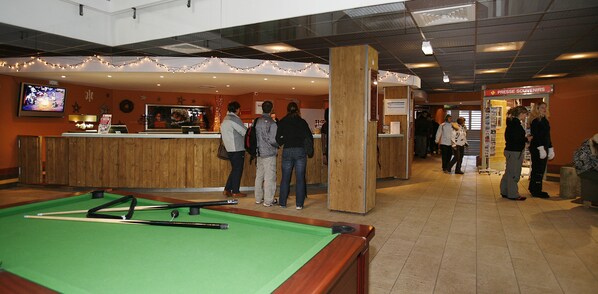 A pool table with cue sticks, a bar area with a TV, and a souvenir press. - Le Schuss (Les Belleville)