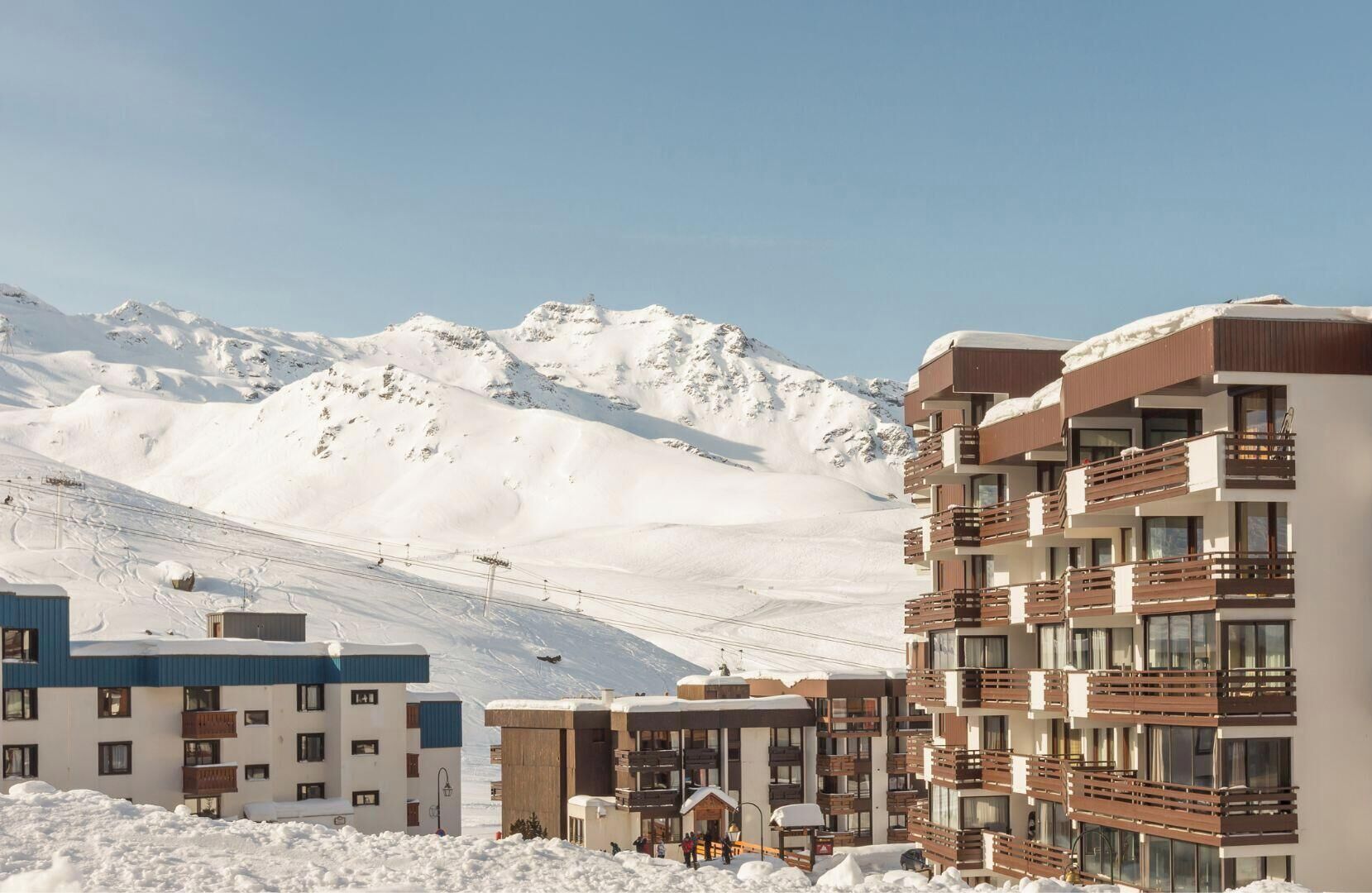 Ein modernes Hotel mit mehreren Etagen, Balkonen und einer verschneiten Berglandschaft im Hintergrund.