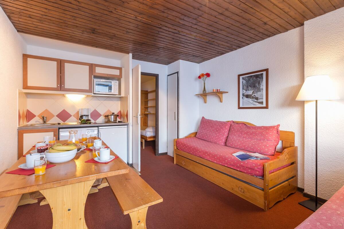 Ein gemütlicher Raum mit einem Holztisch, der für ein Frühstück gedeckt ist, einer Holzsofa, einem Bett, einer Mikrowelle und einem Regal mit einem Bild.