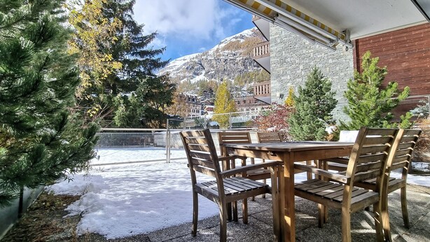 An outdoor seating area with wooden tables and chairs, surrounded by snow-covered ground and trees. - La Villa Emeline - Wohnung Emilie (Zermatt)