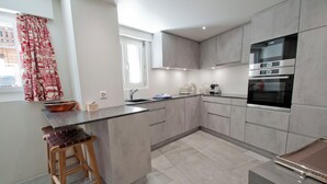 A modern kitchen with grey cabinets, a stainless steel oven, and a wooden stool. - La Villa Emeline - Wohnung Emilie (Zermatt)