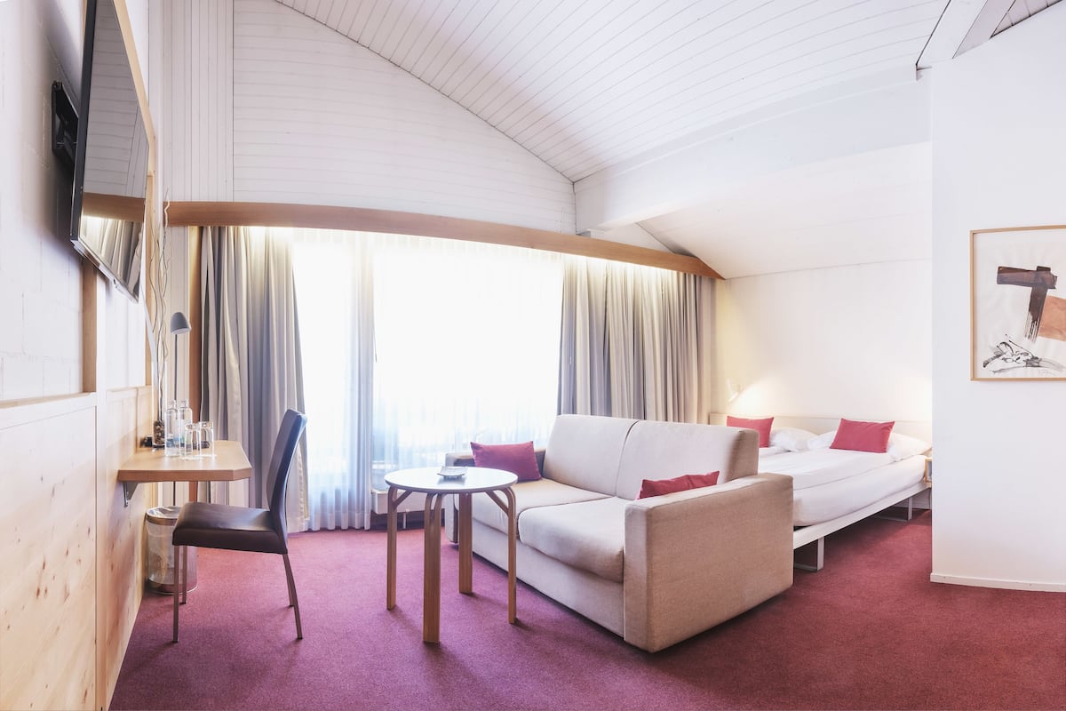A hotel room with a sofa, a small table, a chair, a bed, and a TV mounted on the wall.
