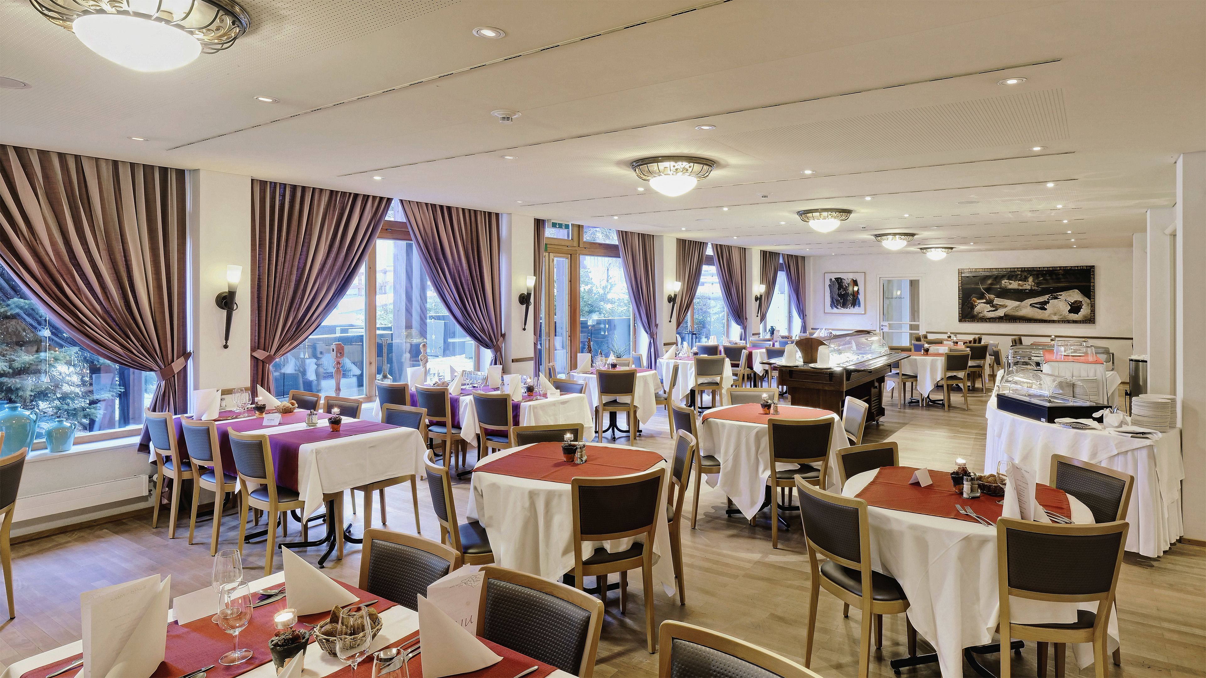 A hotel dining area with multiple tables, chairs, and a buffet setup.