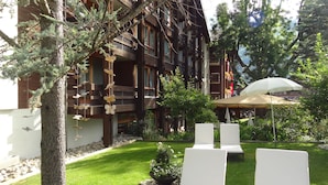 A courtyard with outdoor seating, a building with balconies, and a tree. - Hotel Kreuz Lenk (Lenk)
