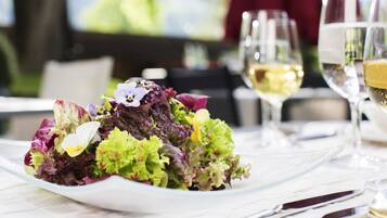 Una mesa dispuesta con ensalada de verduras mixtas, copas de vino y cubiertos.
