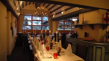 Een restaurant met gedekte tafels, kaarsen op elke tafel en een uitzicht op het buitenleven door grote ramen.