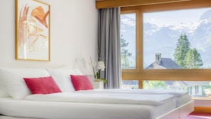 A bedroom with a large bed, a painting on the wall, and a view of mountains through a window. - Hotel Kreuz Lenk (Lenk)