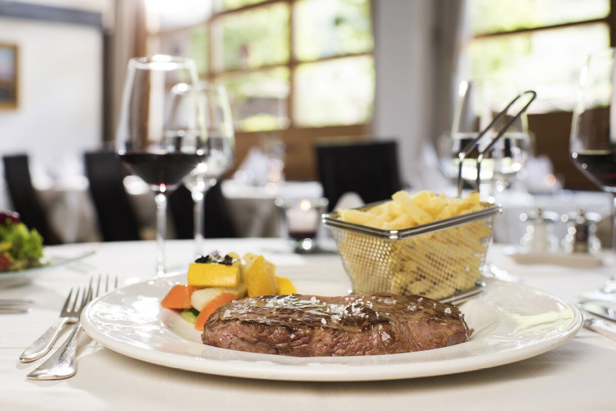 A plate with steak, vegetables, and a basket of fries on a table in a restaurant.