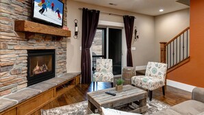 Ein Wohnzimmer mit Kamin aus Stein, zwei gemusterte Sessel, einem Couchtisch und einem Fernseher, der über dem Kamin befestigt ist.