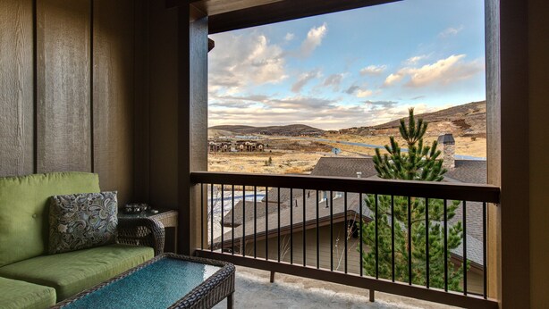 Ein Balkon mit Blick auf eine Berglandschaft, ein Korbstuhl und ein grünes Sofa.