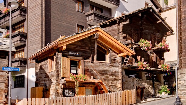 Een houten chalet met een stenen gevel, houten balkons en bloembakken.