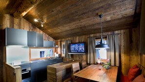 Een houten interieur met een keuken, een eethoek en een aan de muur bevestigde televisie.