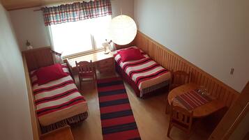 Una habitación pequeña y acogedora con dos camas individuales, un escritorio de madera, una silla y una mesita con una lámpara.
