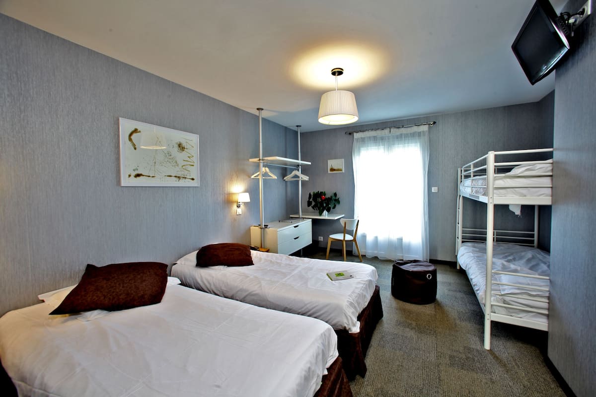 A hotel room with two beds, a desk, a chair, a TV, and a bunk bed.