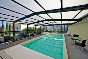 An indoor swimming pool with a glass ceiling, surrounded by lounge chairs and tables, and a restaurant in the background. - Logis L'auberge de Moricq (Angles)
