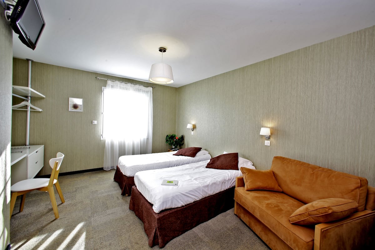 A hotel room with two single beds, a sofa, a desk, and a TV.