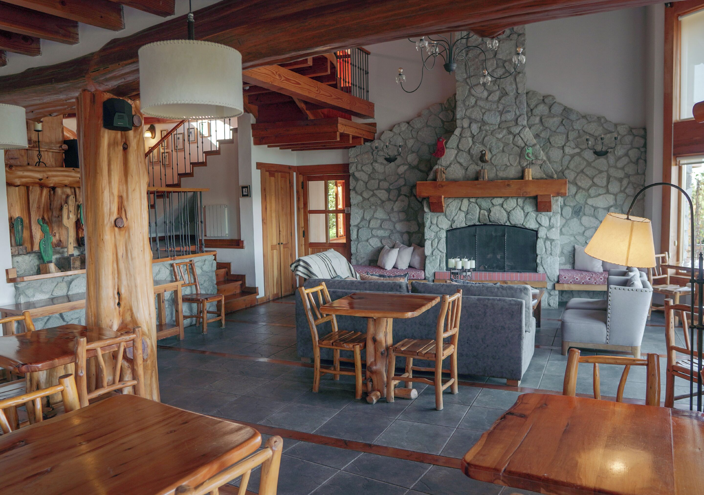 A spacious living area with a stone fireplace, wooden furniture, and a staircase leading to an upper level.